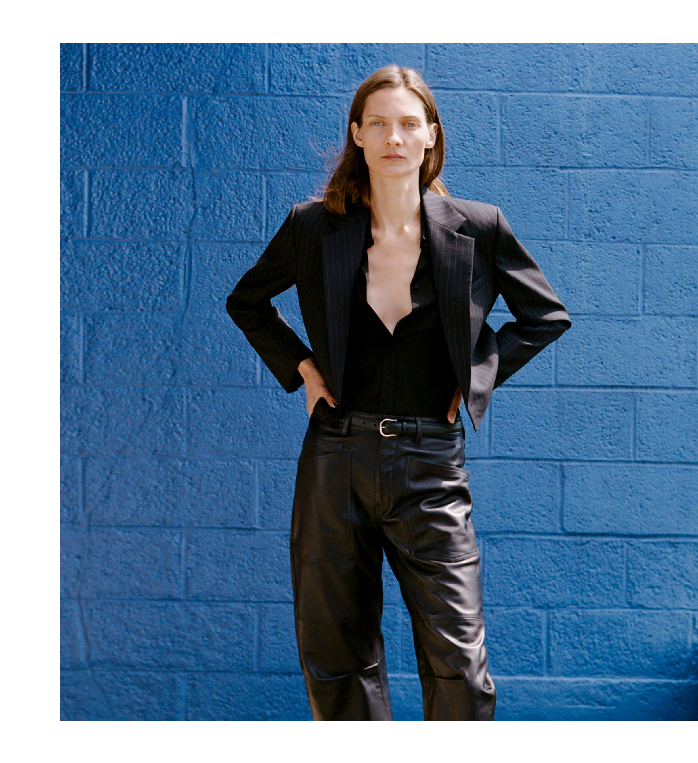 Woman in a black outfit standing against a blue wall.