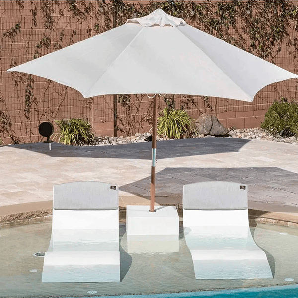 In-pool side table with umbrella stand and concrete chaise lounge chairs on pool tanning ledge.