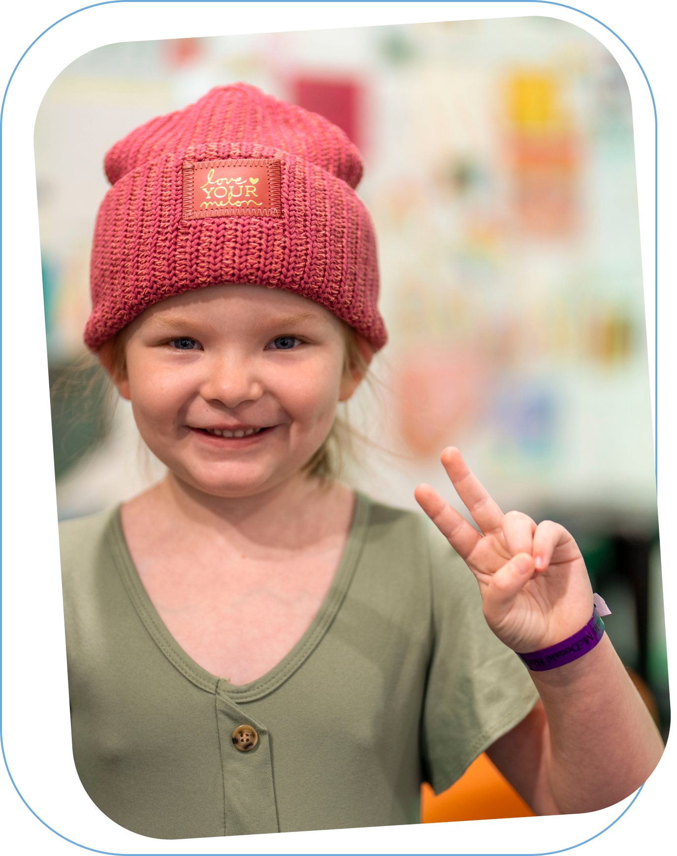 Young girl wearing a pink Love Your Melon beanie smiling while holding up a peace sign