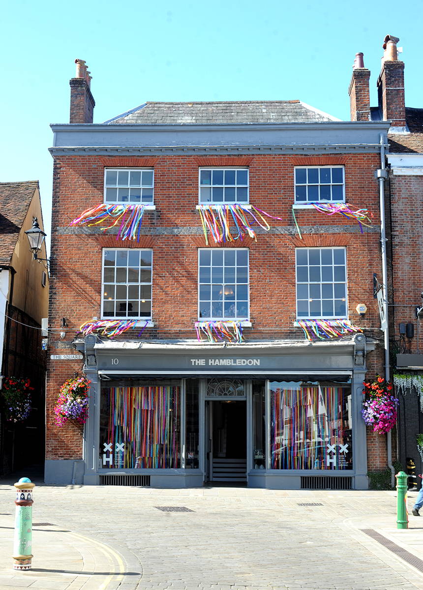 An image of The Hambledon shop front with colourful streamers displayed in the windows.