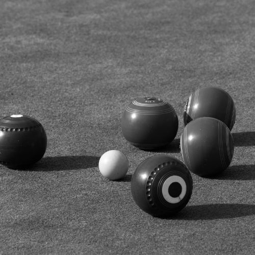 Various colored lawn bowls scattered on a green surface.