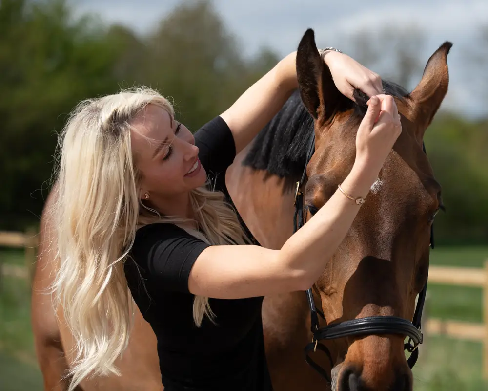 Woman using BEAUTIFY OIL on her horse in a sunny outdoor setting.