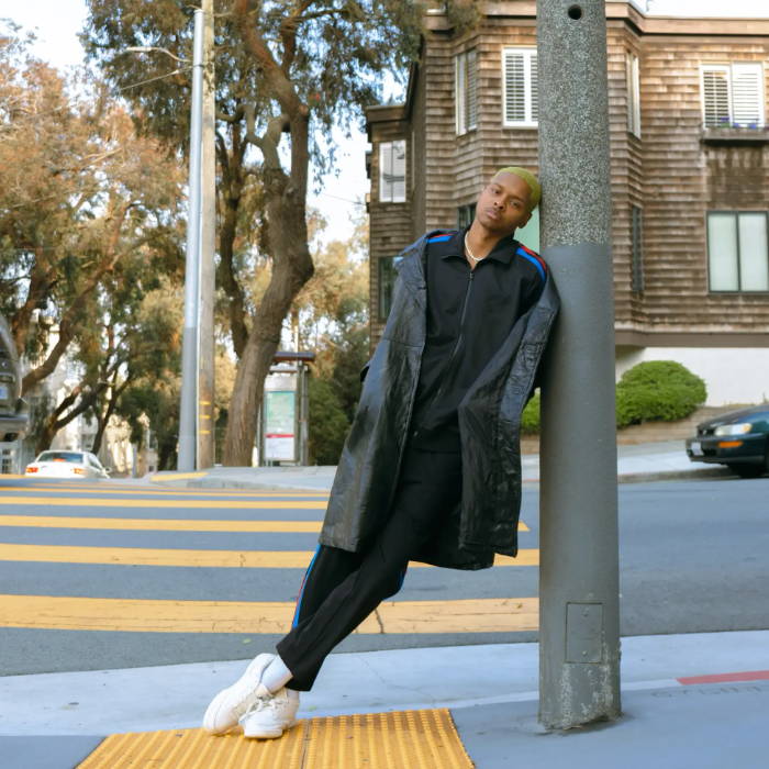male model in maison article track suit leaning against street pole
