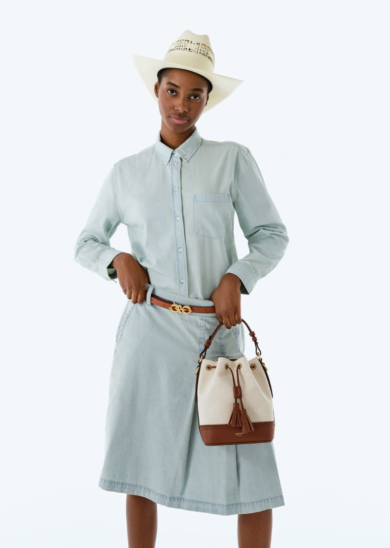 Person in a light blue dress holding a handbag, wearing a straw hat.