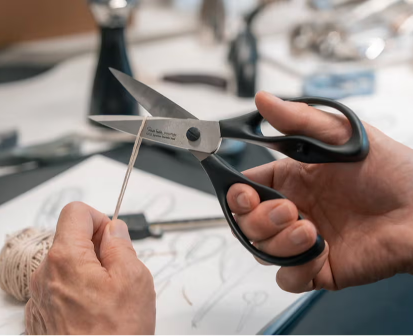 A person using Signature Scissors to cut a piece of string.