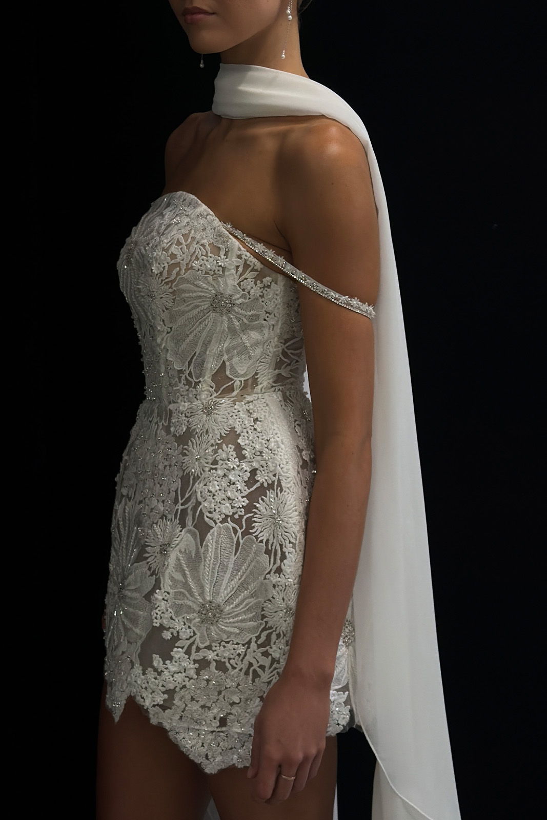 Woman wearing a lace, strapless dress with a flowing white scarf.