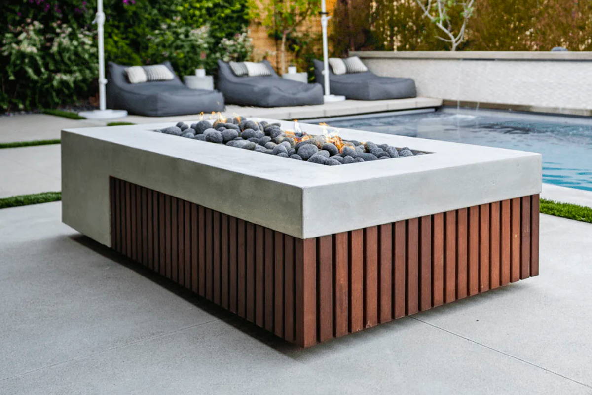 A stylish GFRC fire pit made of wood and concrete, placed adjacent to a pool, creating a perfect outdoor ambiance.