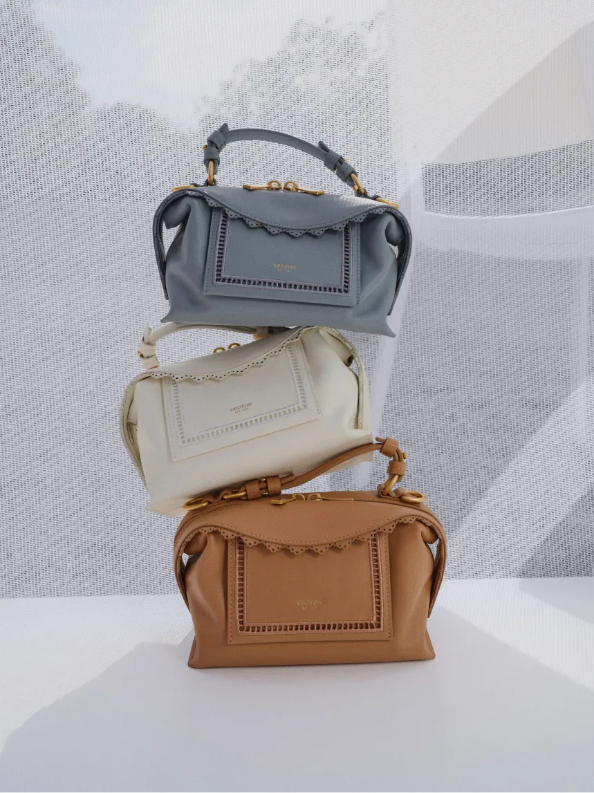 Three stylish handbags in gray, white, and brown stacked together.
