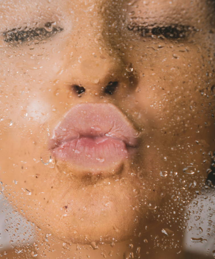 A woman kissing a pane of glass. The glass is covered in water droplets