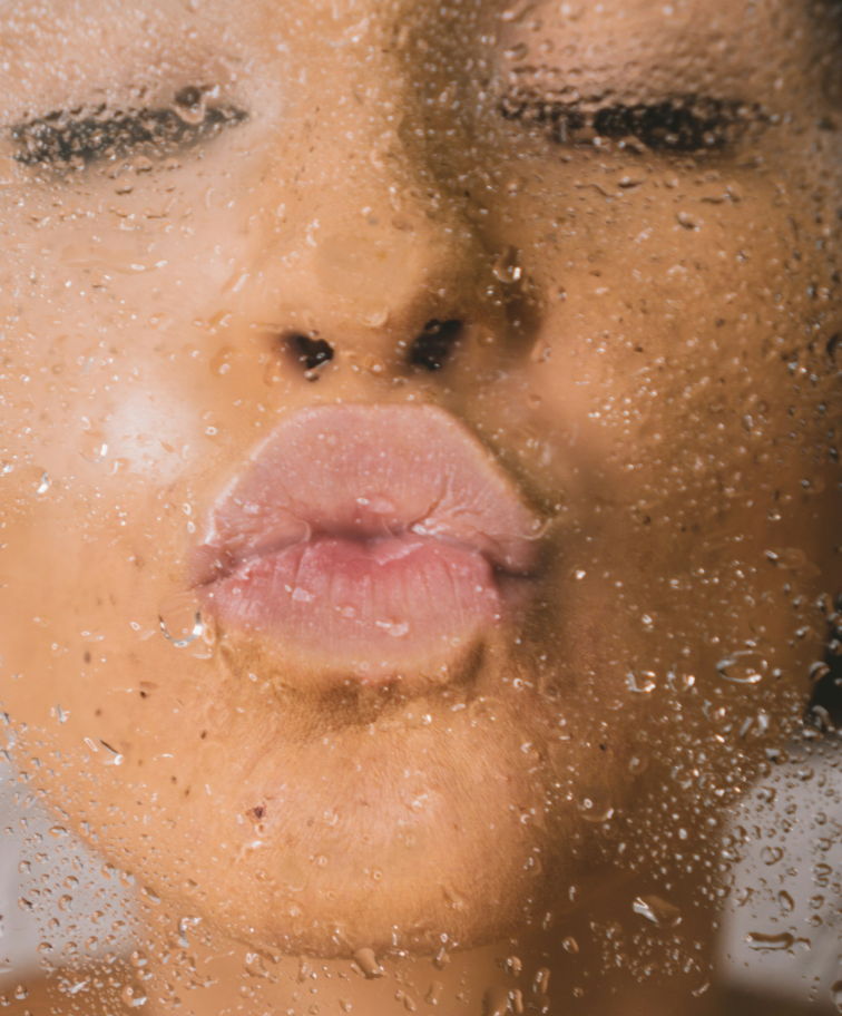 A woman kissing a pane of glass. The glass is covered in water droplets