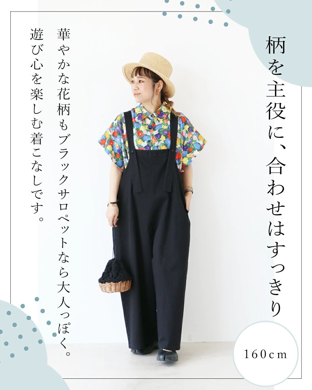 Woman in colorful shirt and black overalls, wearing a hat.