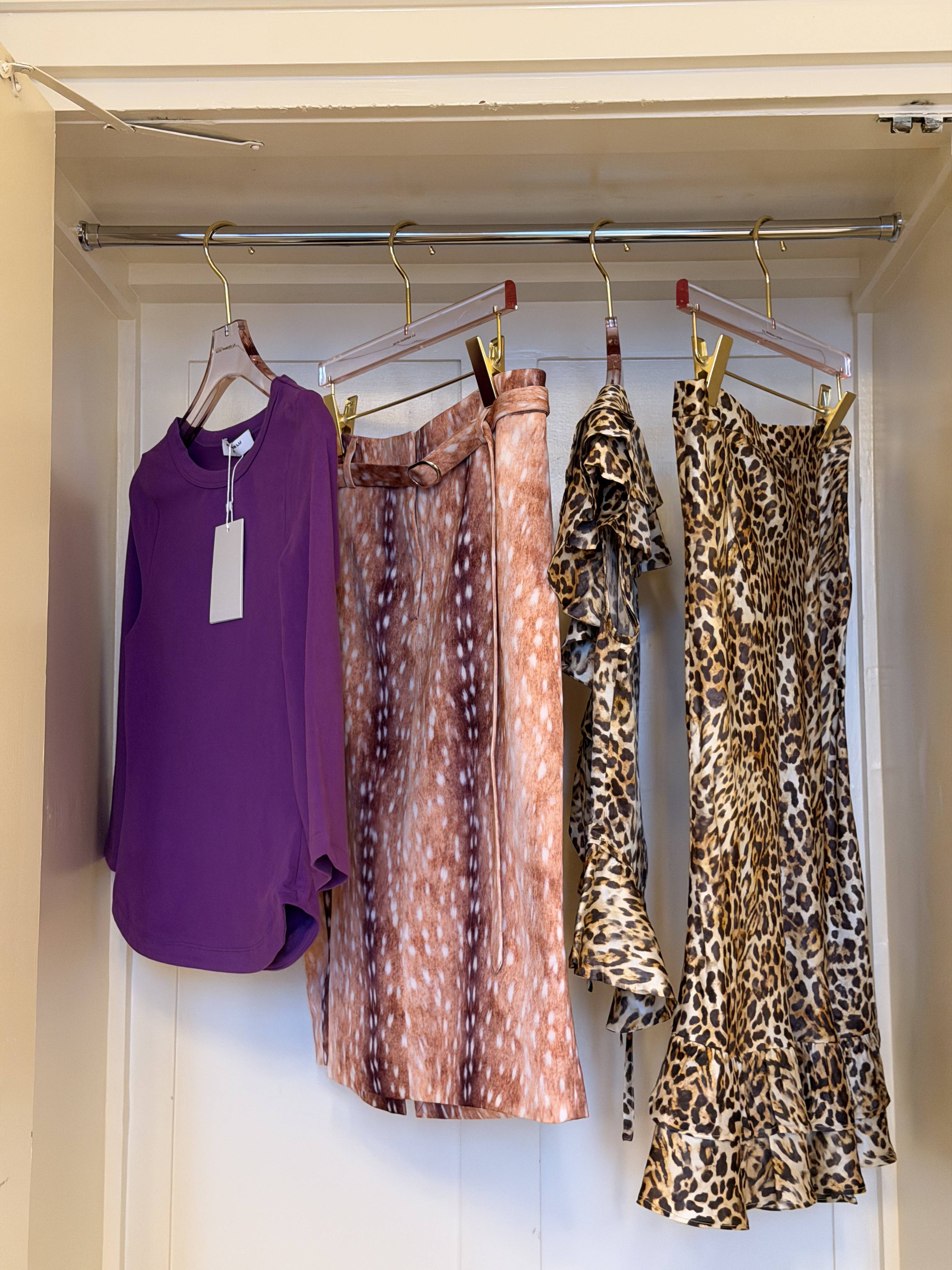 Four stylish garments hanging in a closet: a purple top, patterned skirts, and a dress.