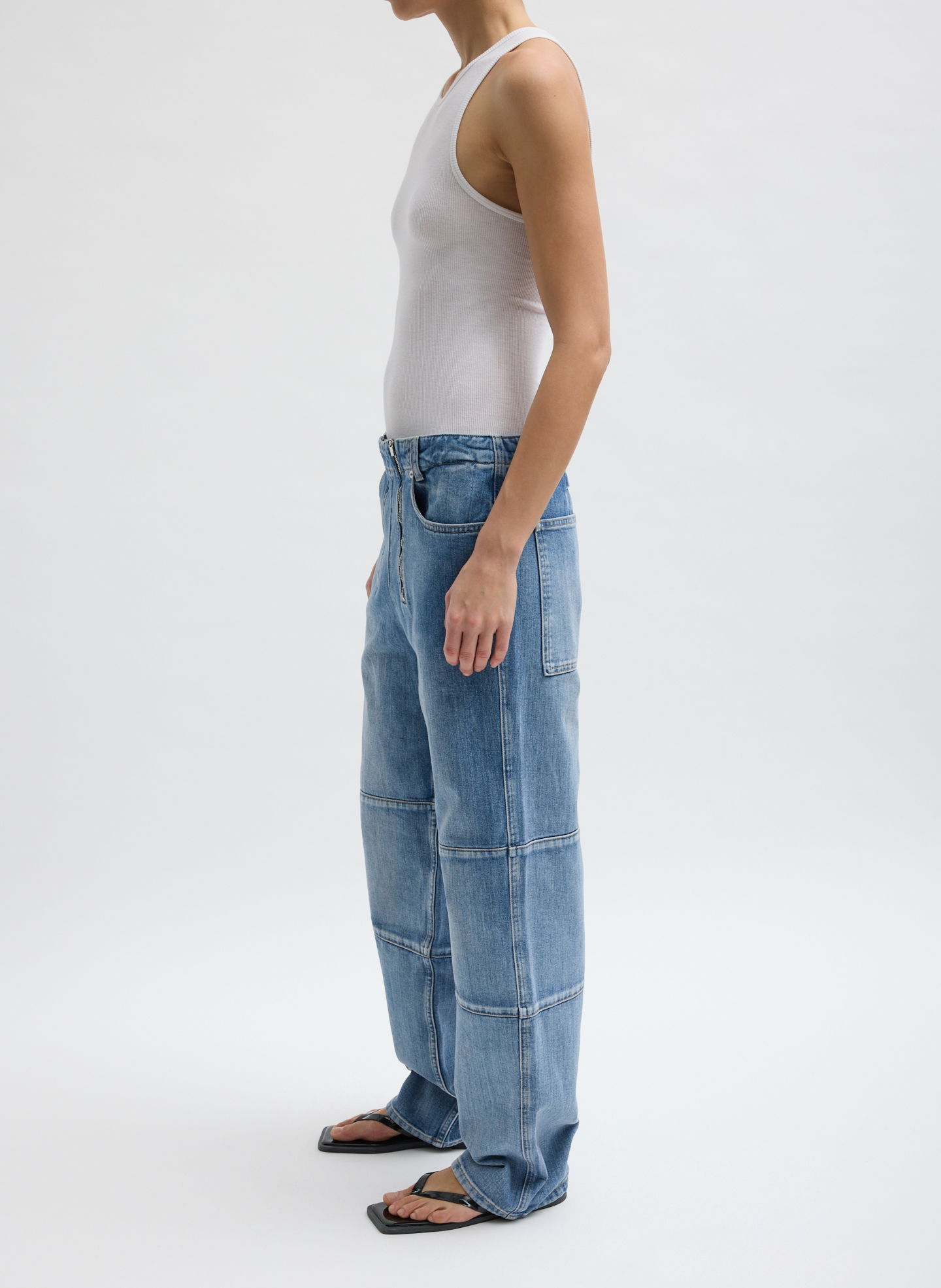 Person wearing a white tank top and blue baggy jeans, standing sideways.