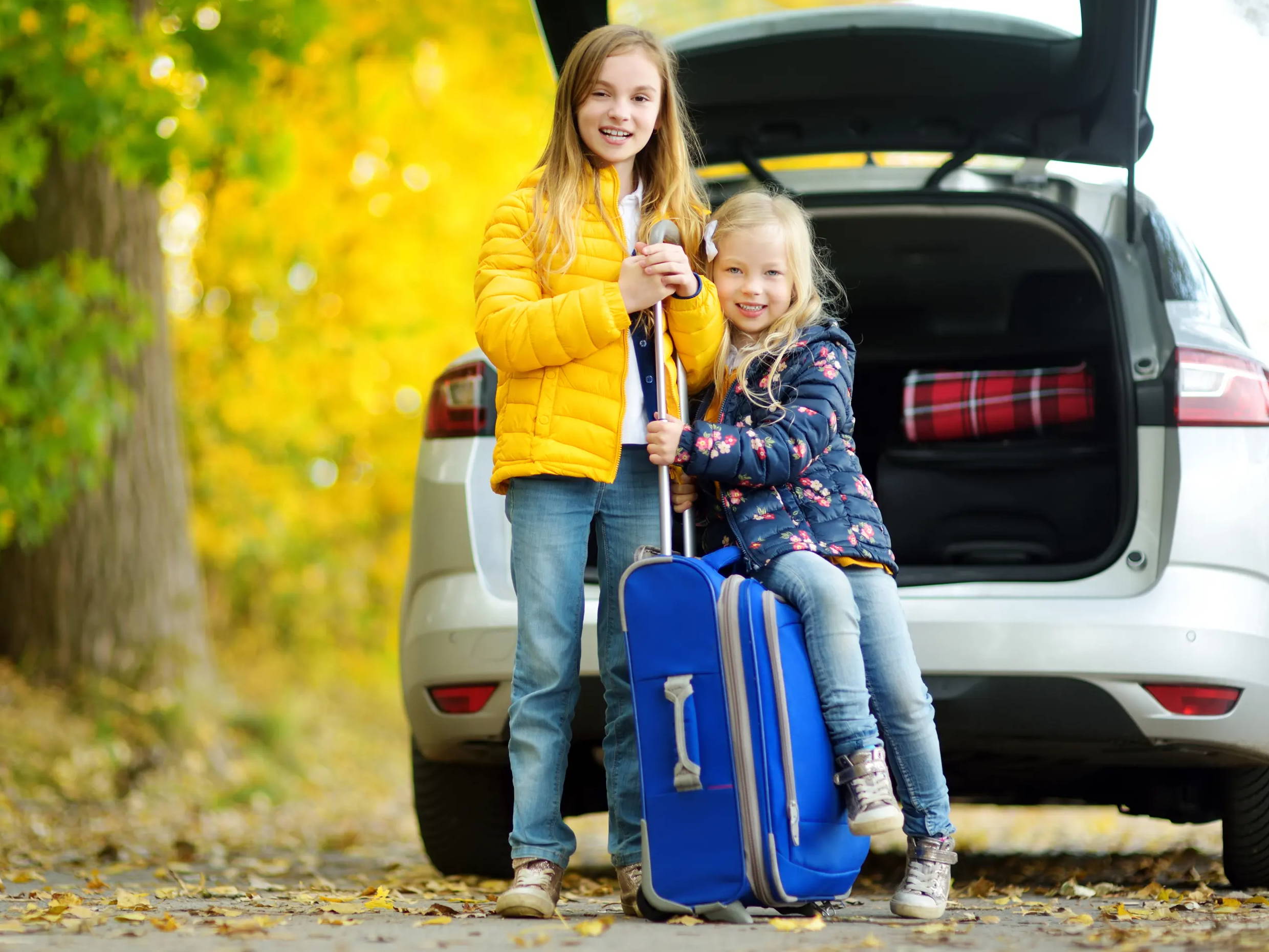 kids next to car with suitcase in the fall