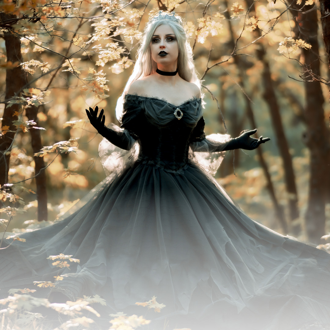 A woman in a black gown stands in a forest with autumn leaves.
