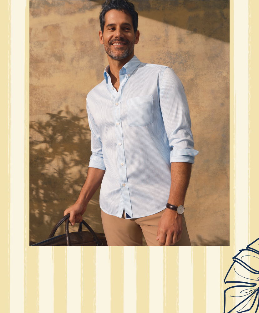 Smiling man in light blue shirt holding a bag outdoors.
