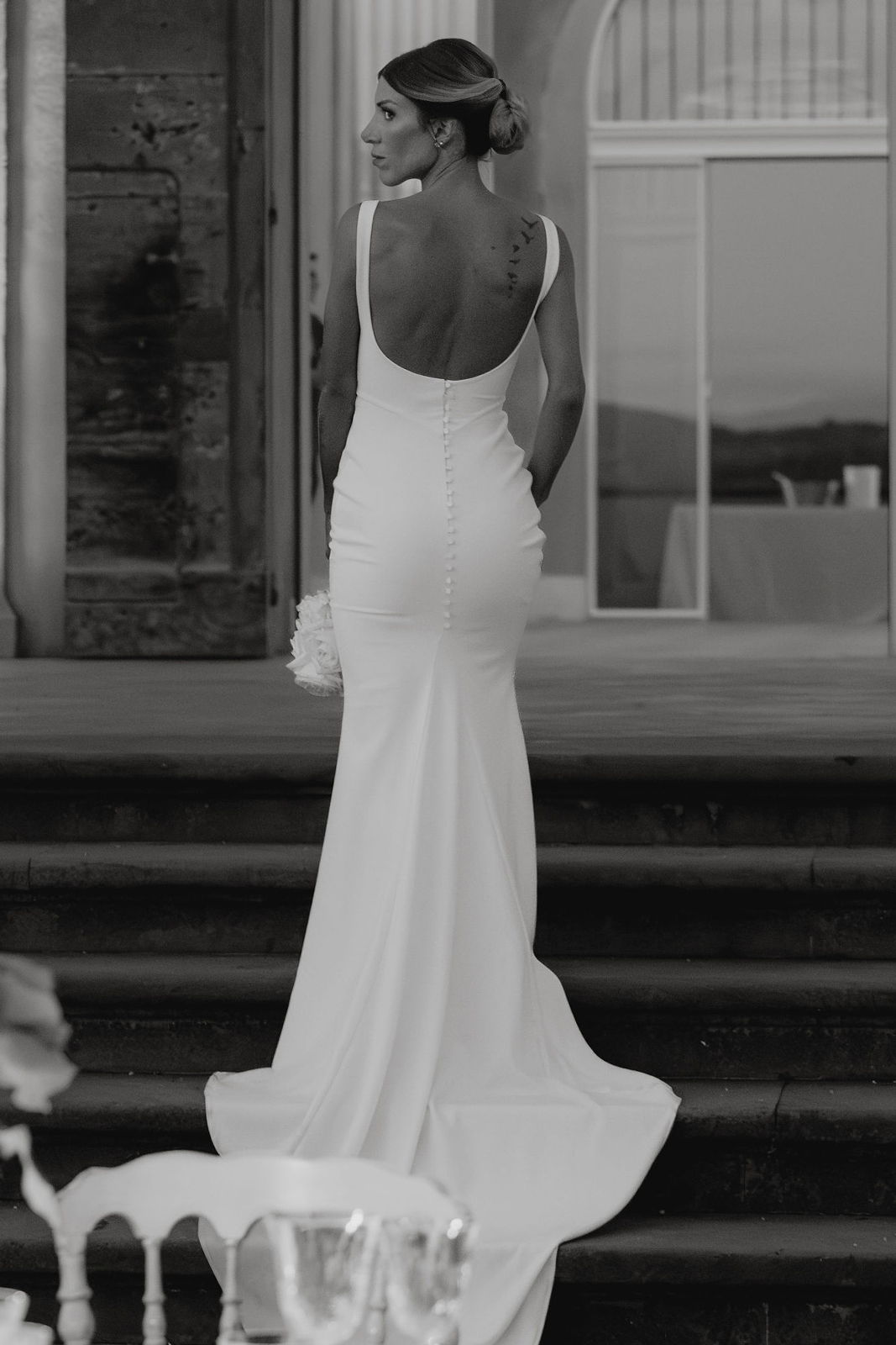 Woman in a white dress walking away, viewed from behind.
