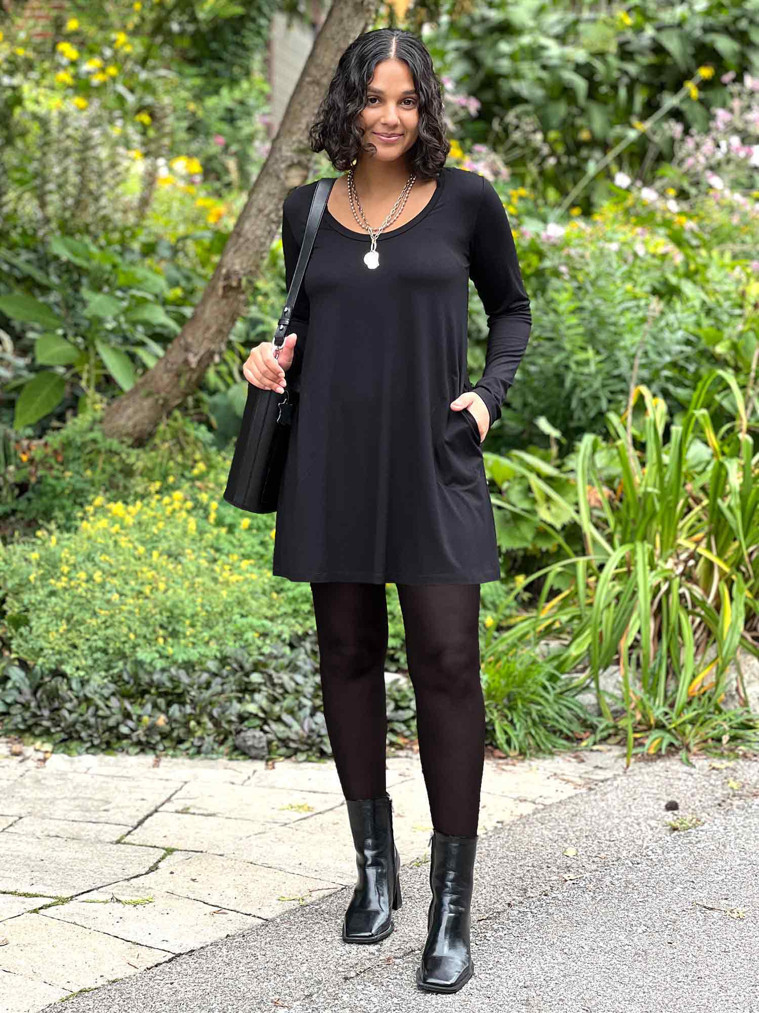 Woman standing wearing Miik's Zuri long sleeve pocket tunic in black with leggings