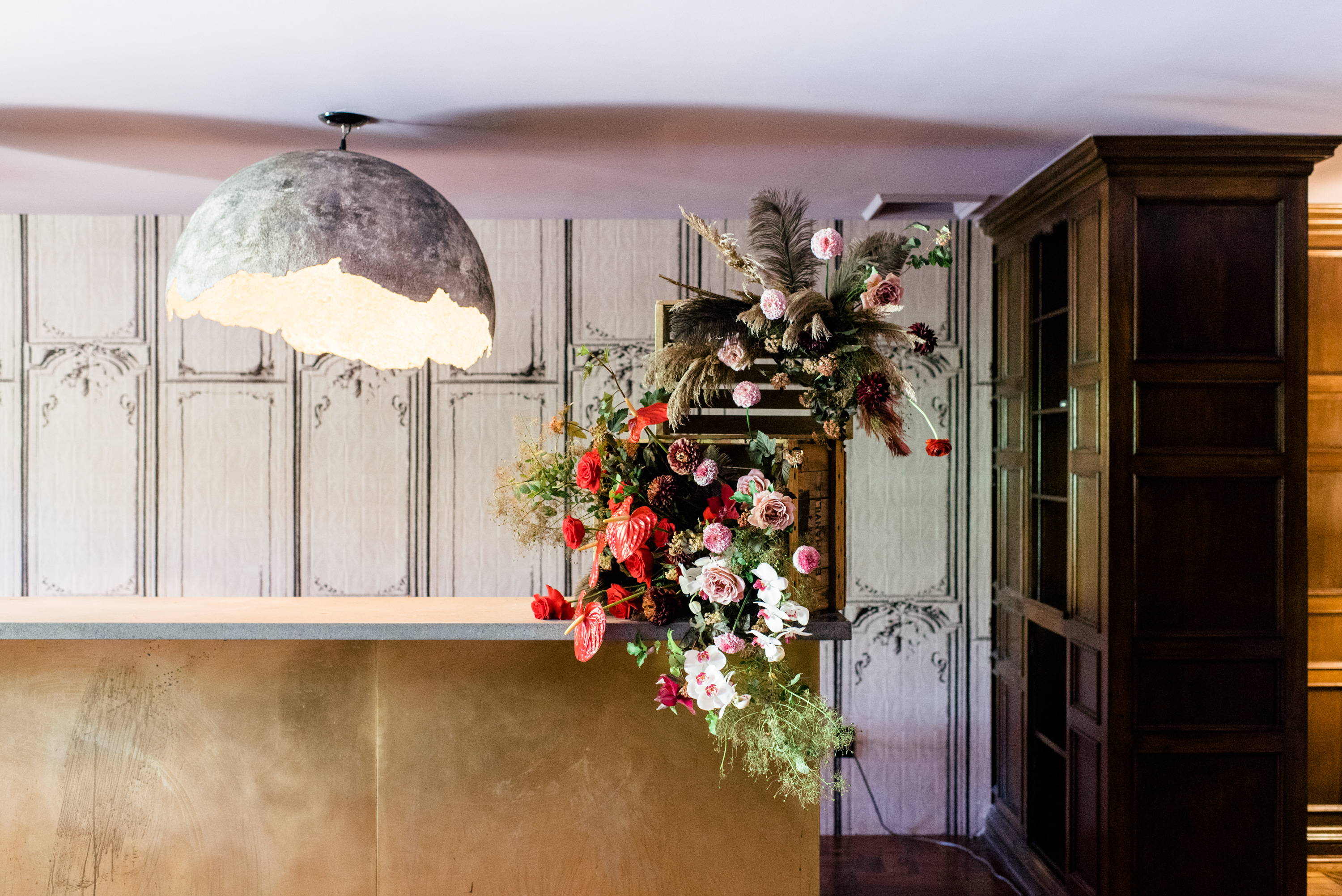 unique floral arrangement with pink and red florals , brown pampas grass in two bar crates on a bar with a cracked egg over head light 