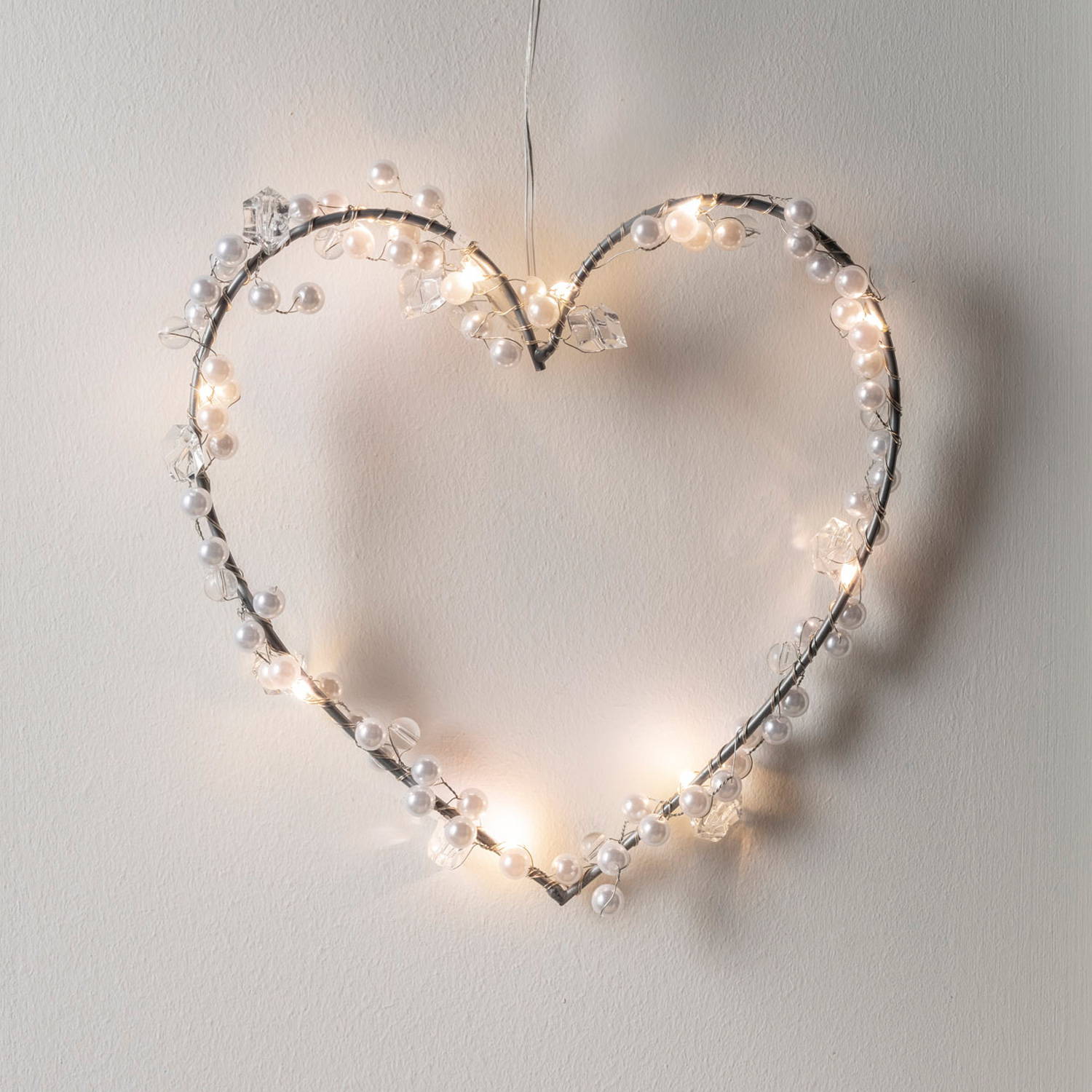 A beaded silver heart light against a white wall.