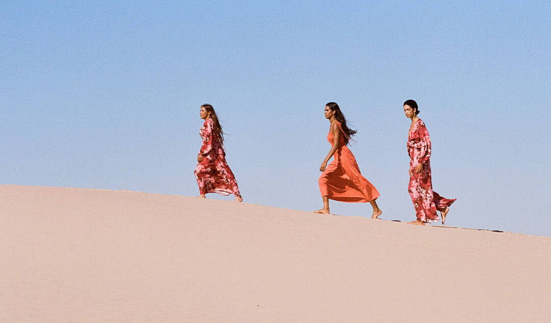 KIVARI Elara Collection | Models and Elder wearing KIVARI red and floral outfits walking across sand
