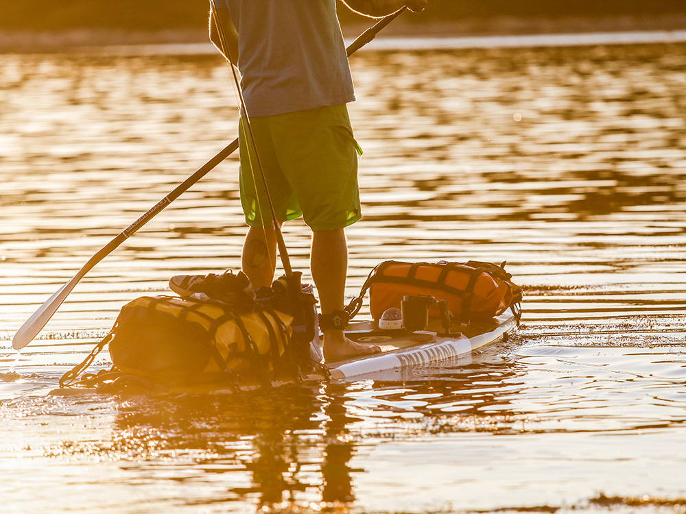 A man paddling a paddleboard loaded with overnight gear