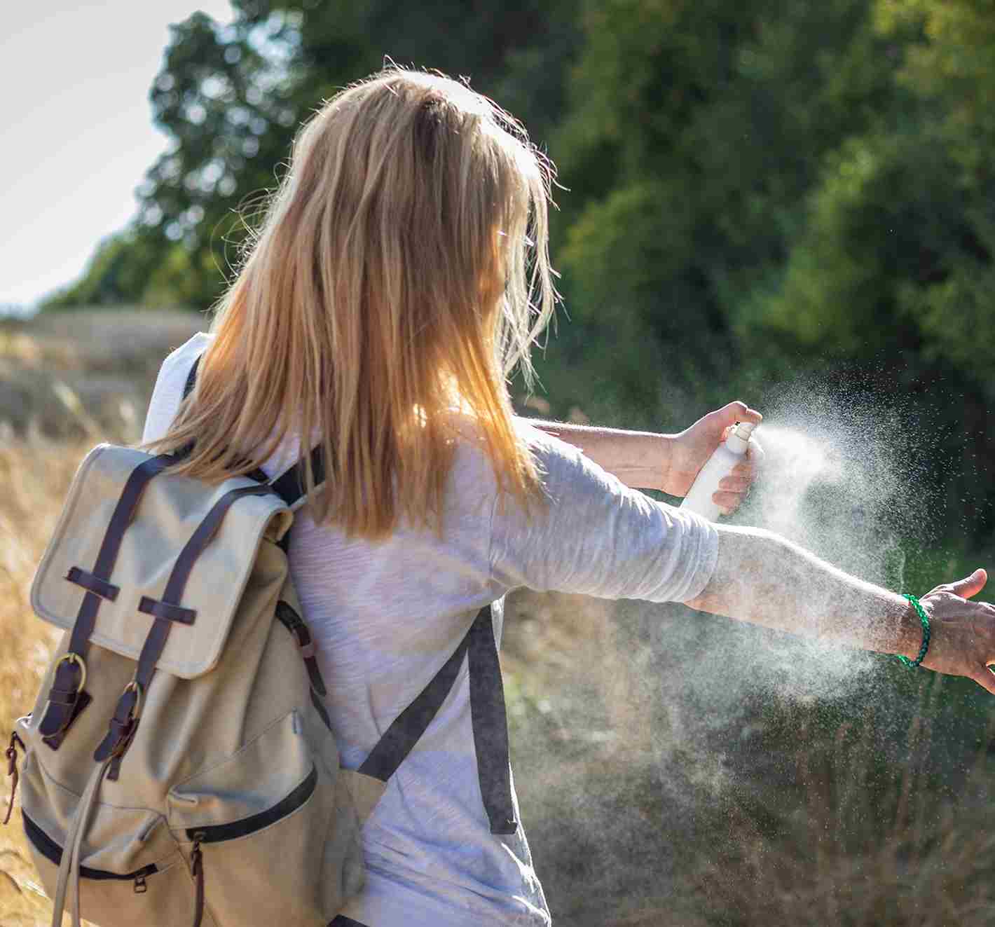  Was ist eine Insektenbissallergie? Junge Frau auf einer Sommerwanderung, die Insektenschutzmittel auf ihren Arm sprüht, um Bisse und so auch Symptome zu vermeiden.