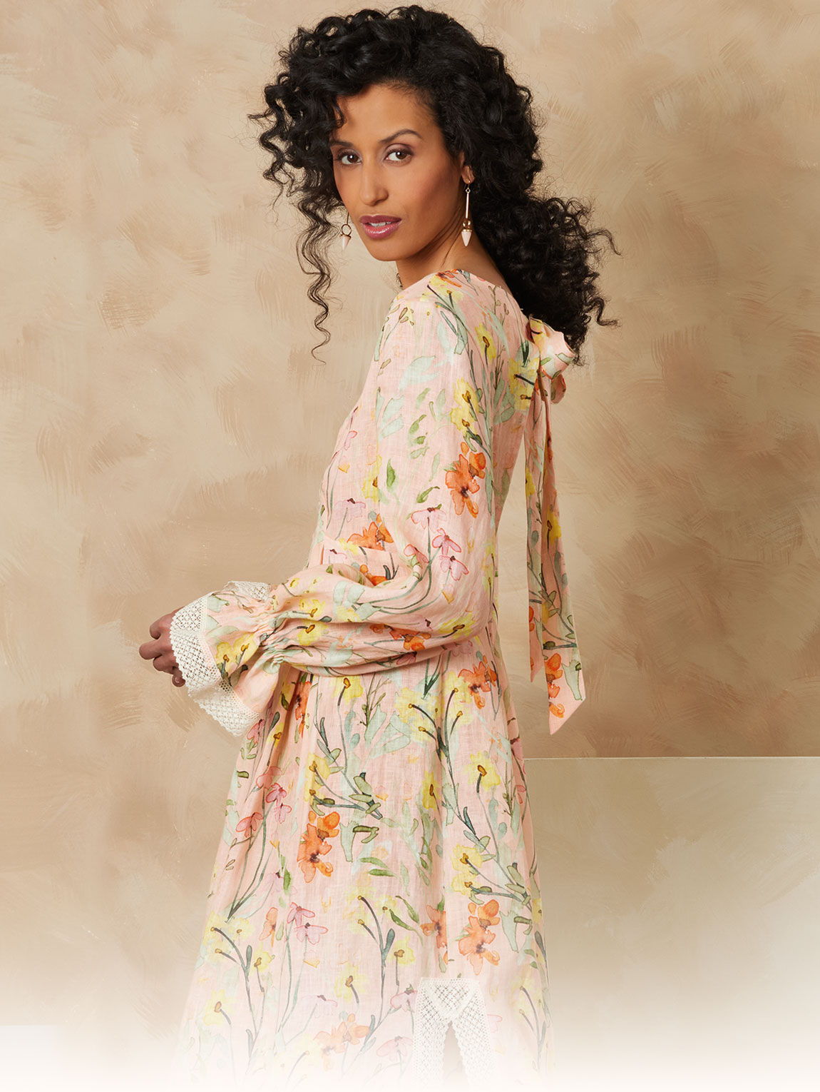 Model in floral dress with curly hair against a soft background.
