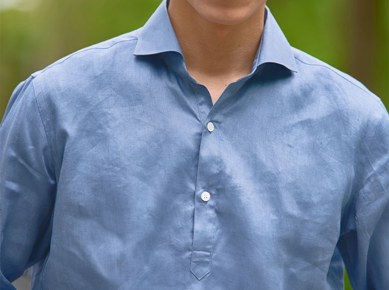 A person wearing a light blue shirt outdoors, with a blurred background.