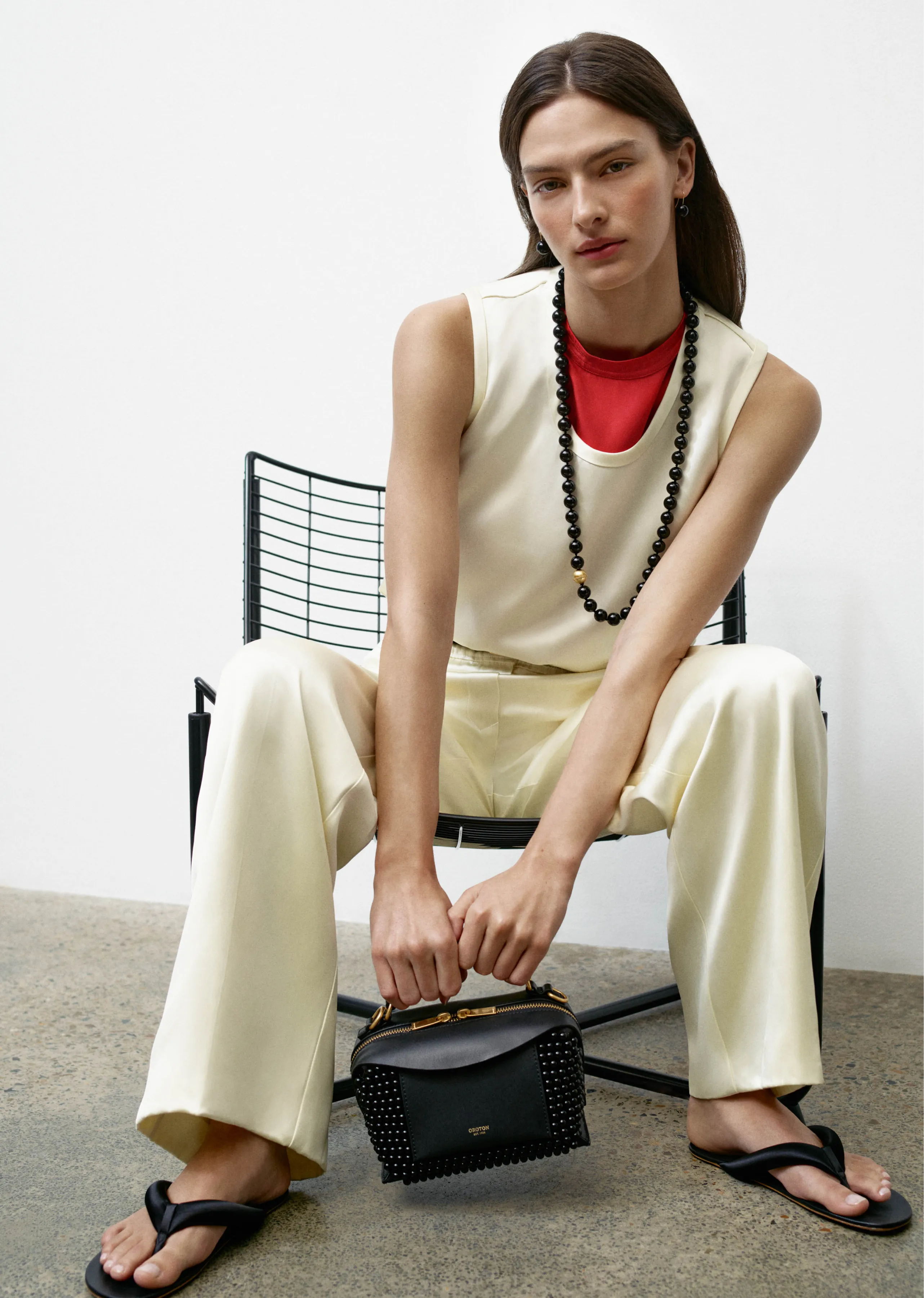 Model in stylish outfit seated on chair, holding a small handbag.