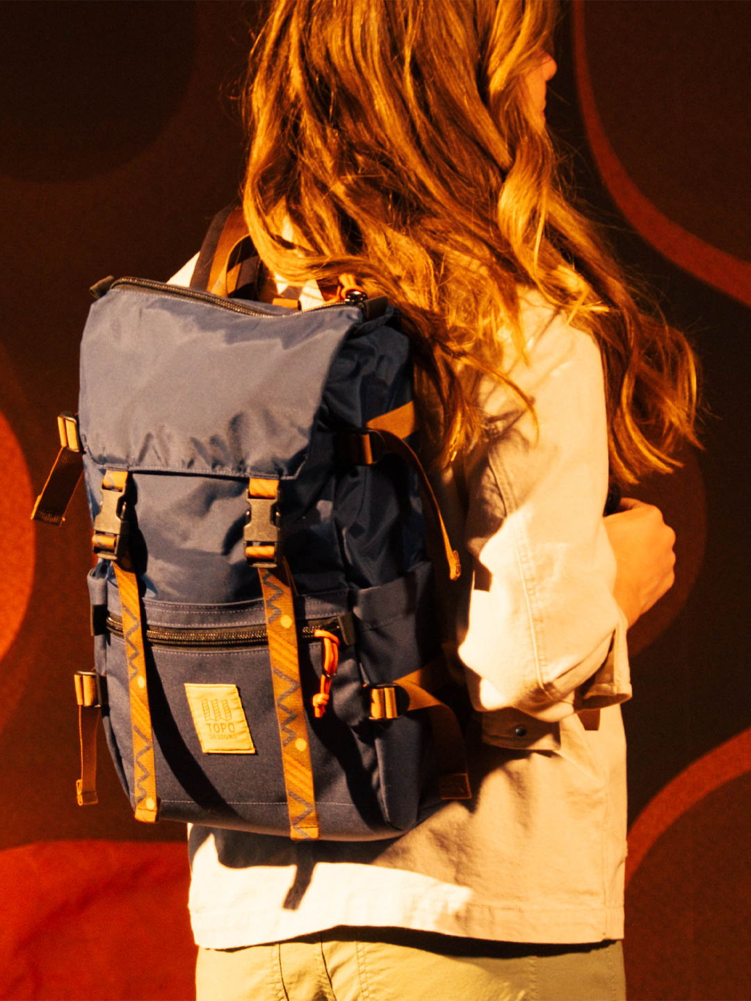 Person with long hair wearing a blue backpack against a colorful background.