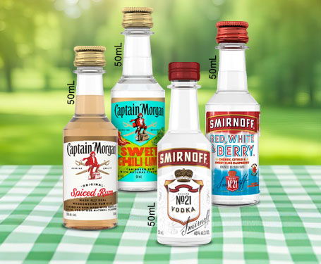 Four bottles of flavored vodka on a green checkered tablecloth outdoors.
