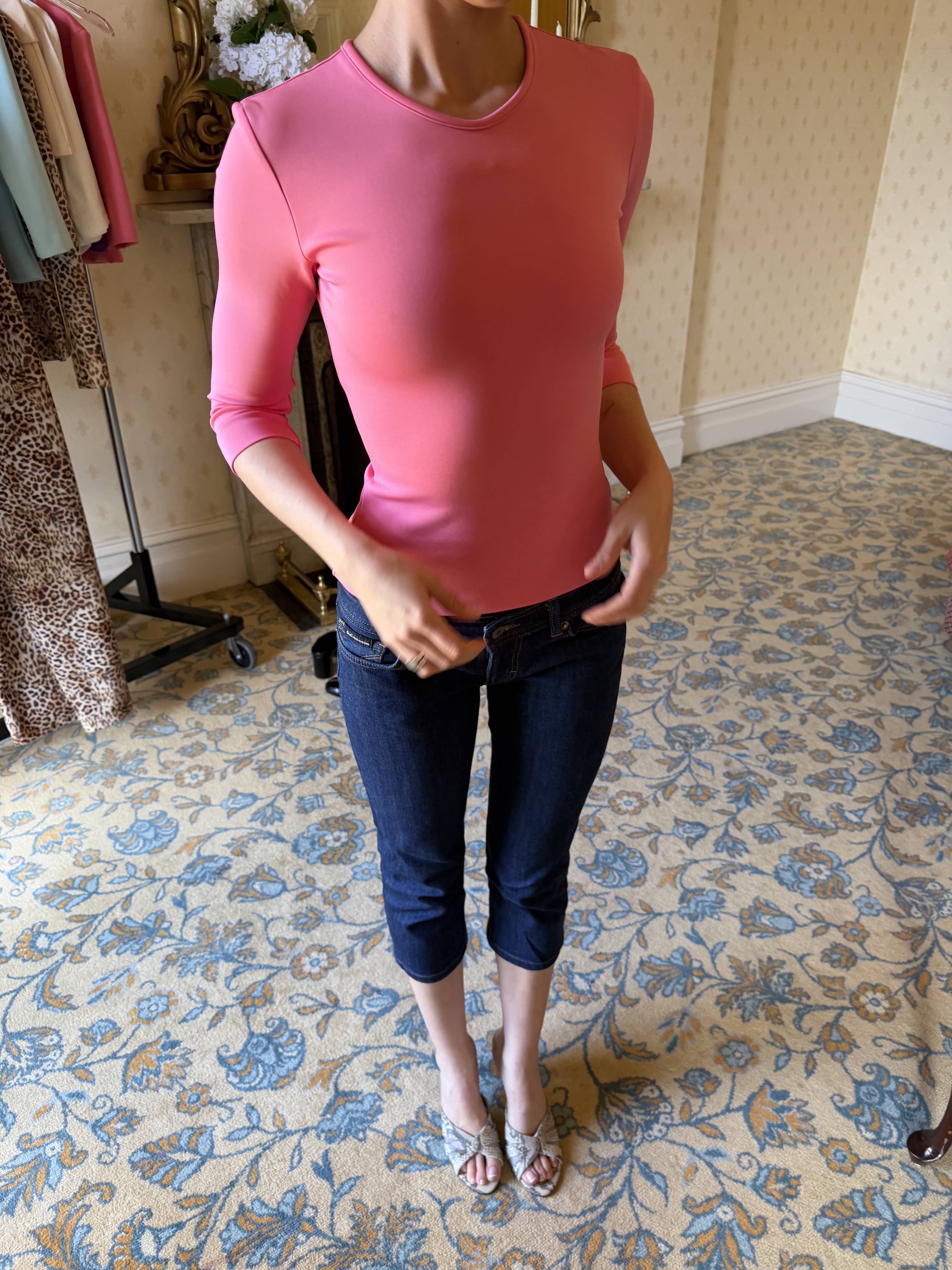 Person wearing a pink shirt and dark pants, standing on patterned carpet.