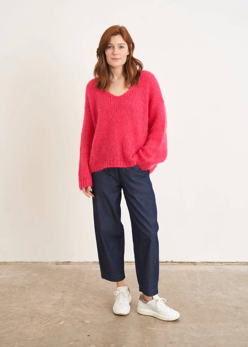 A model wearing a pink chunky knit relaxed fitting sweater with v neckand blue barrel leg jeans with white trainers 