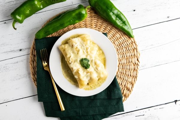 Plate of enchiladas with green sauce and peppers on a woven placemat.