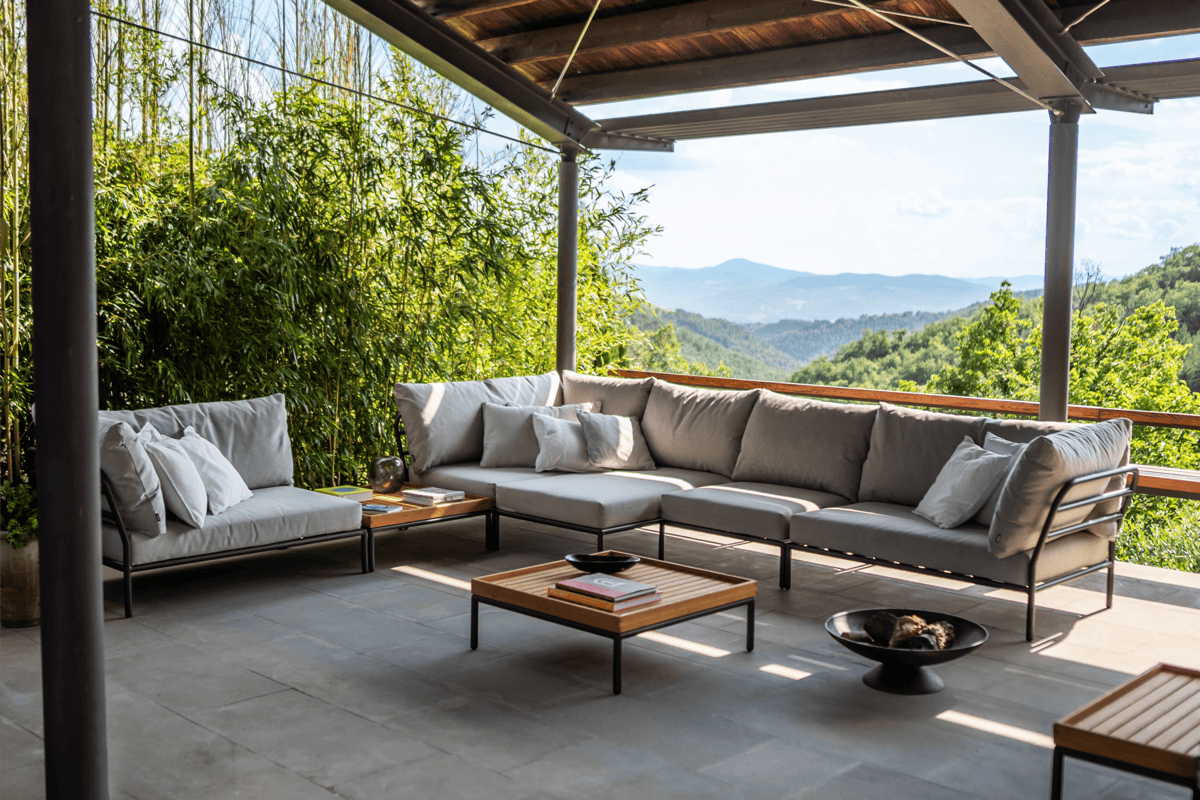 Modern outdoor sectional sofa with gray performance cushions under a covered patio, paired with teak coffee tables and mountain views.