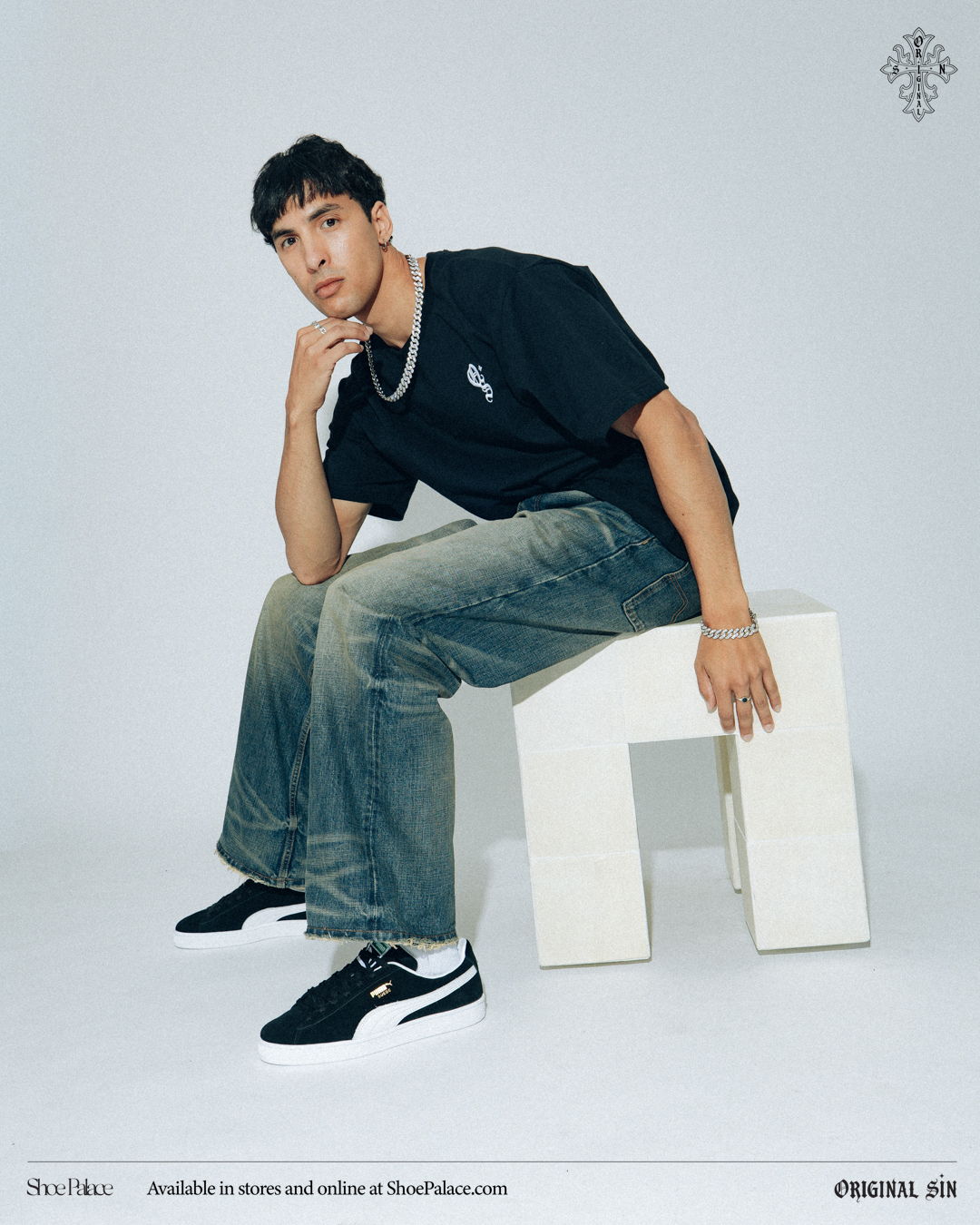 Young man in casual outfit sitting on a block, against a plain background.