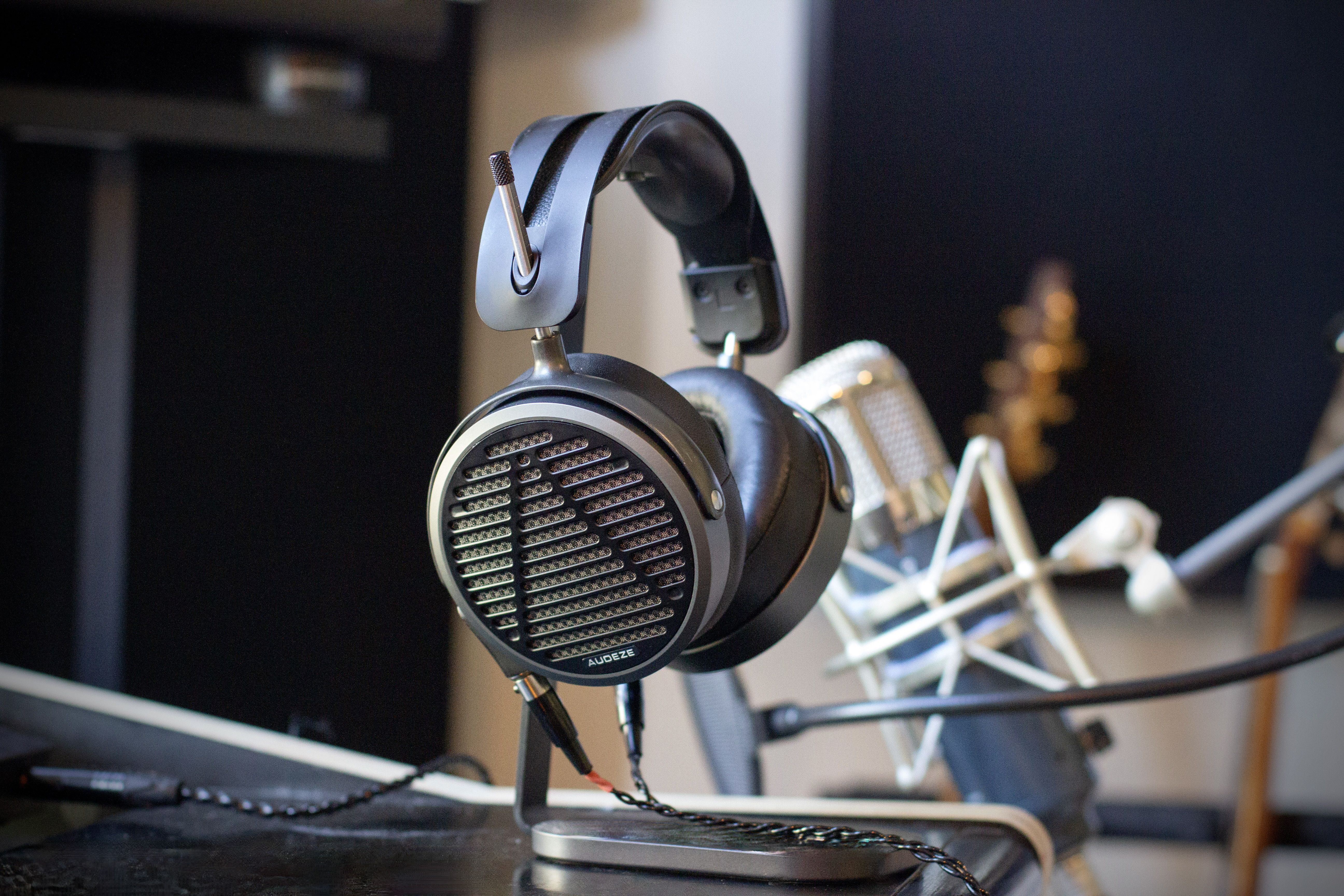 Audeze MM-500 headphones resting on a table with a microphone and guitar in the background.