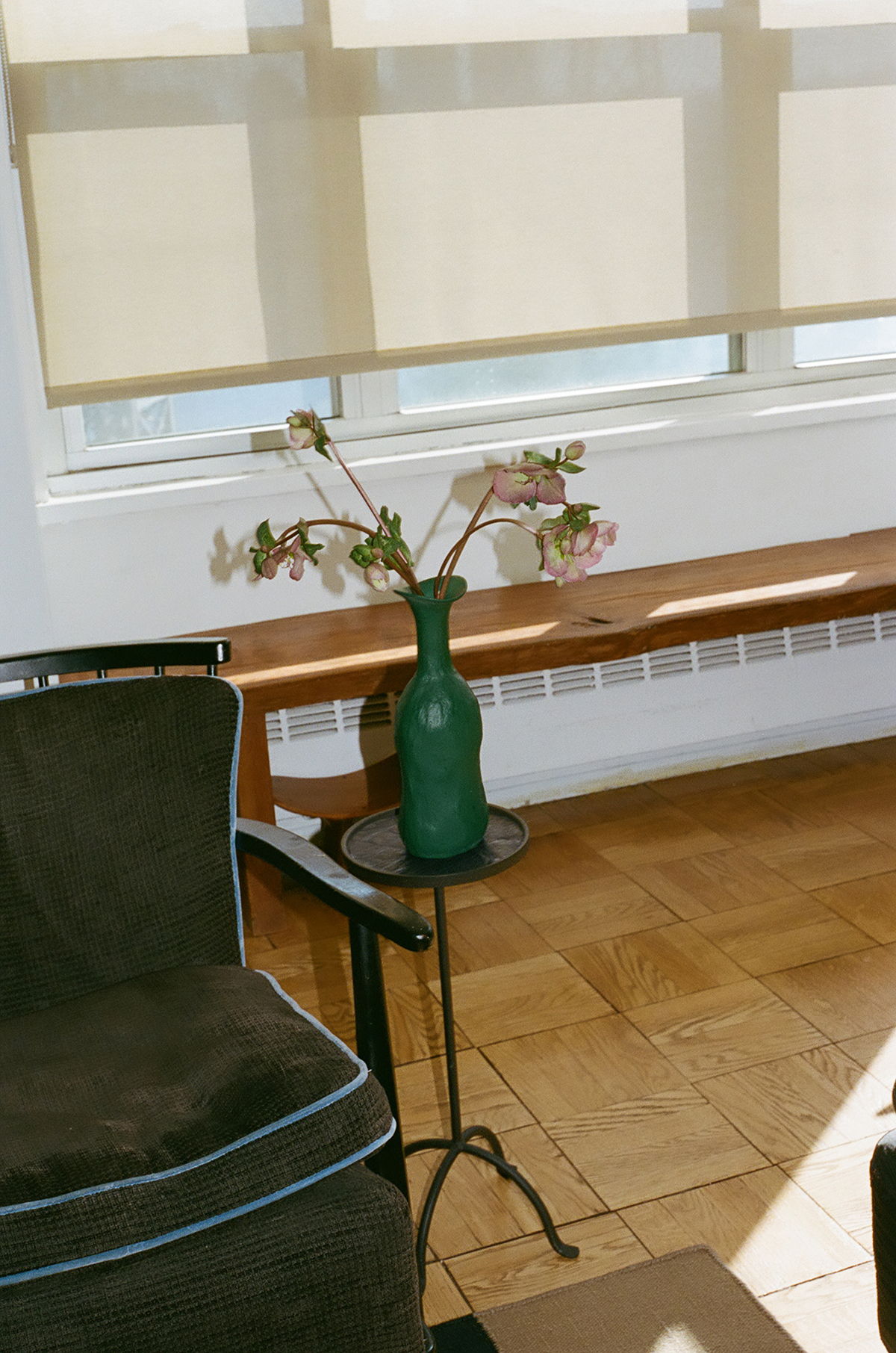 A green vase with flowers on a small table in a sunlit room.