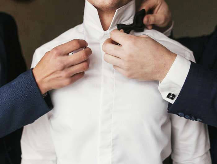 Main in white dress shirt putting on a black bow tie