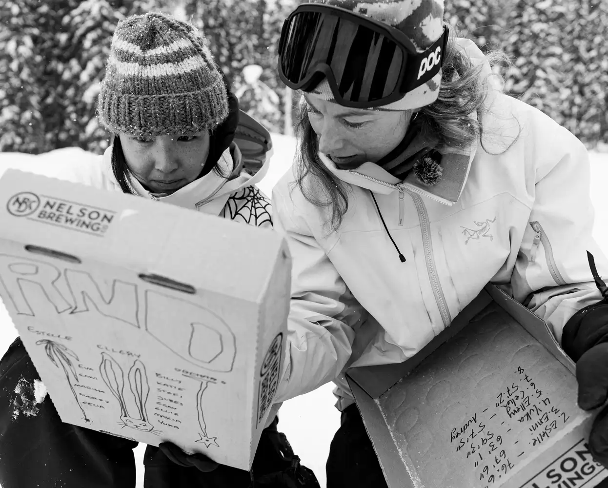 Two people examining a cardboard box in a snowy environment.
