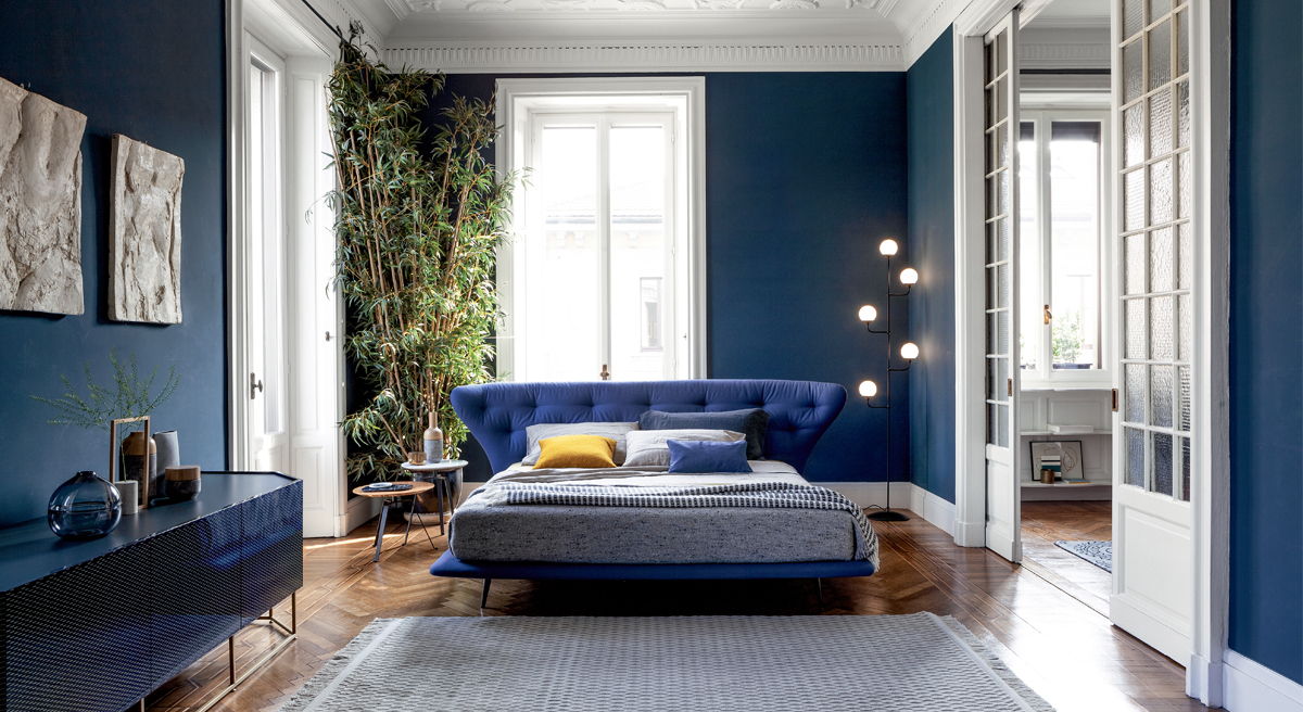 Modern bedroom with blue walls, a bed, and decorative plants.