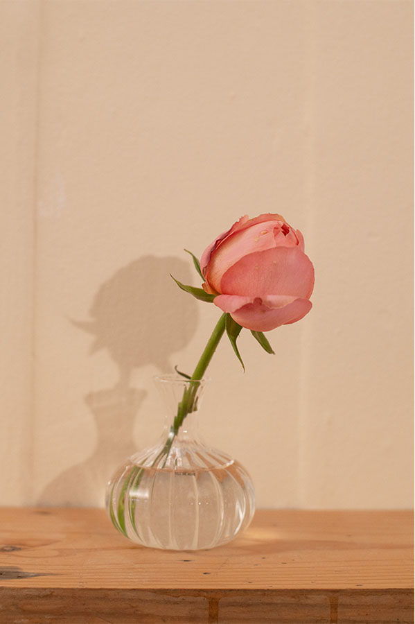 A pink rose in a clear vase on a wooden surface.