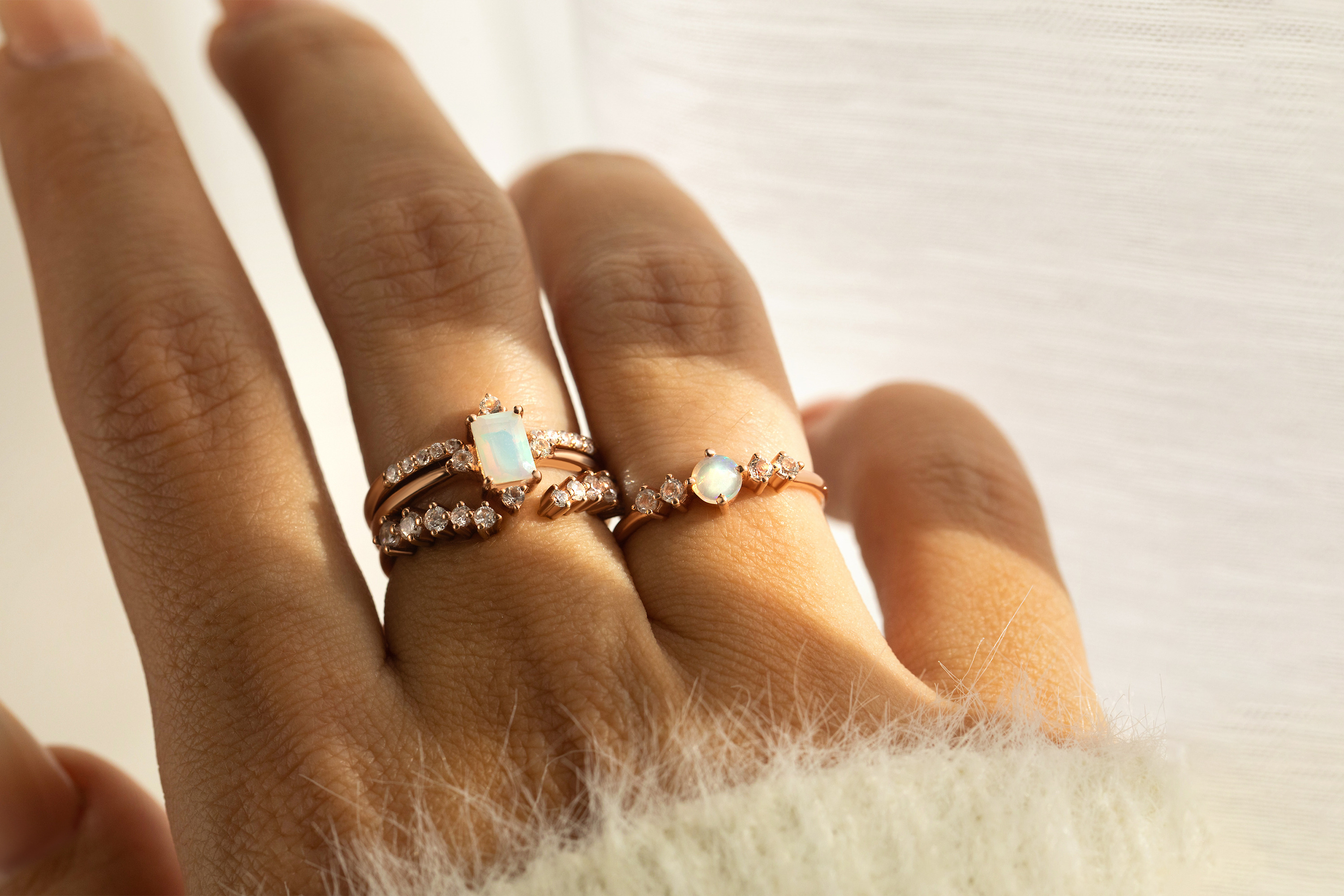 Two Opal rings and two band rings in different styles are presented on a hand.