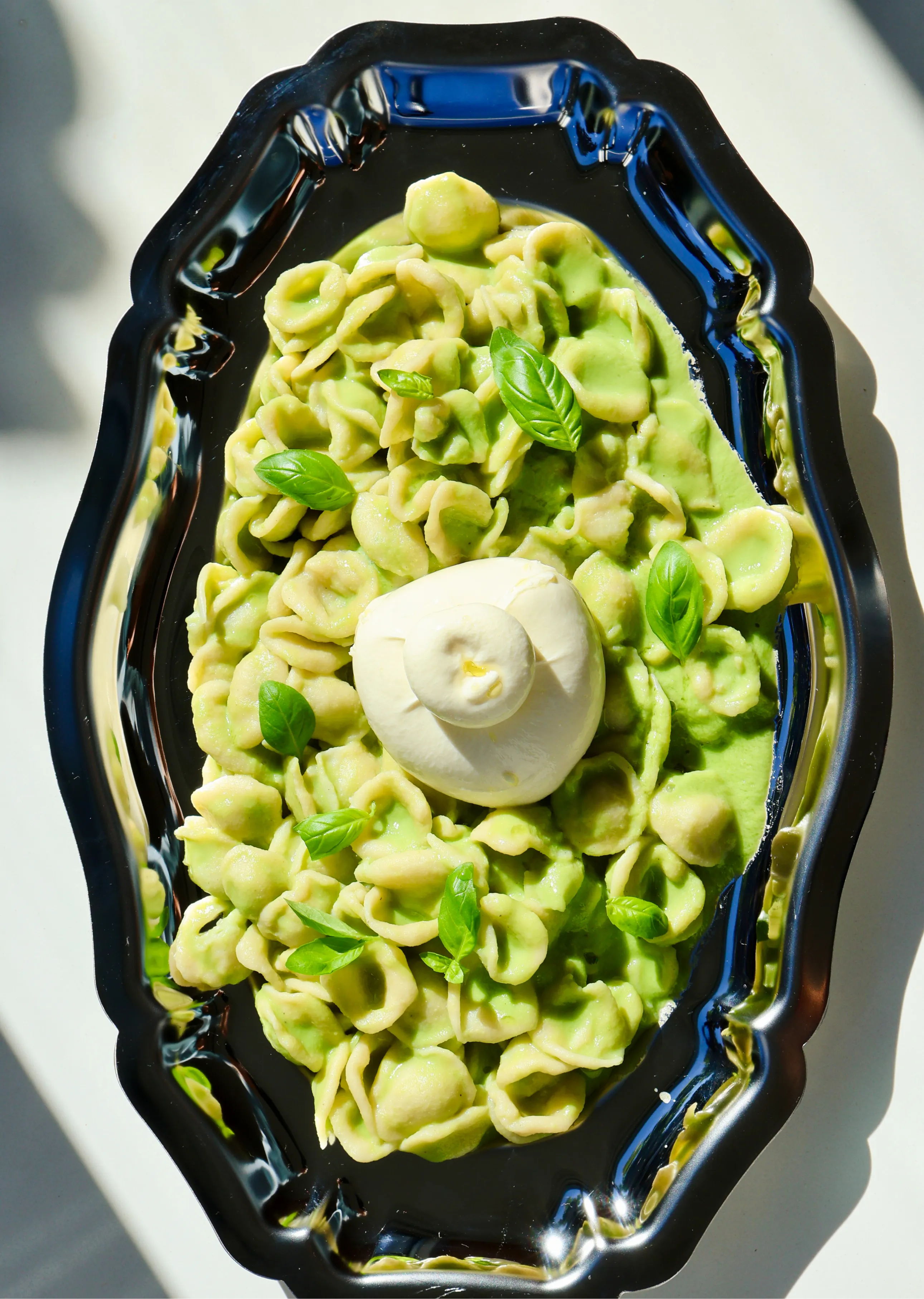 Plate of green pasta with a dollop of cream and garnished with basil.