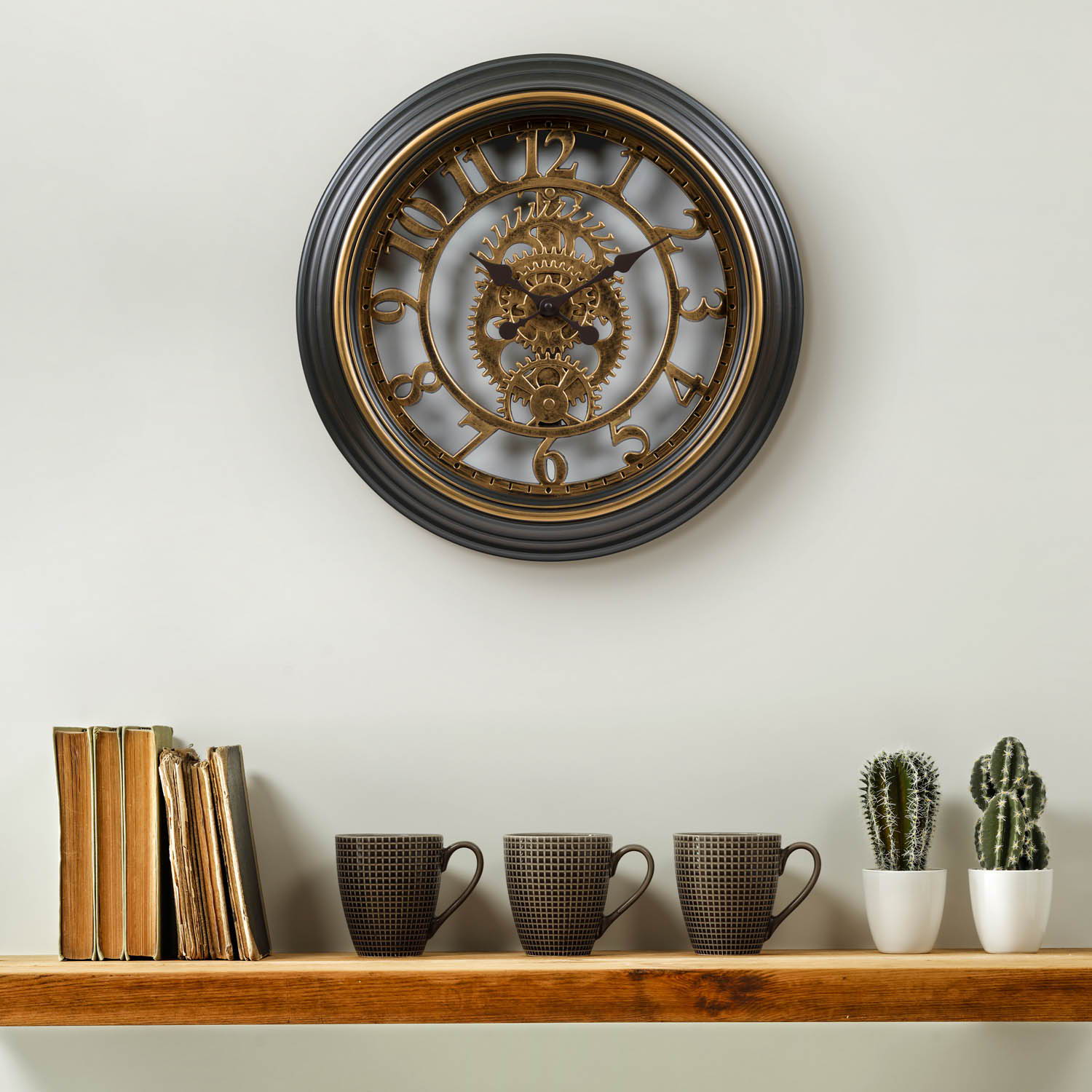 A Gears Clock hanging above a shelf with books, mugs, and cacti.