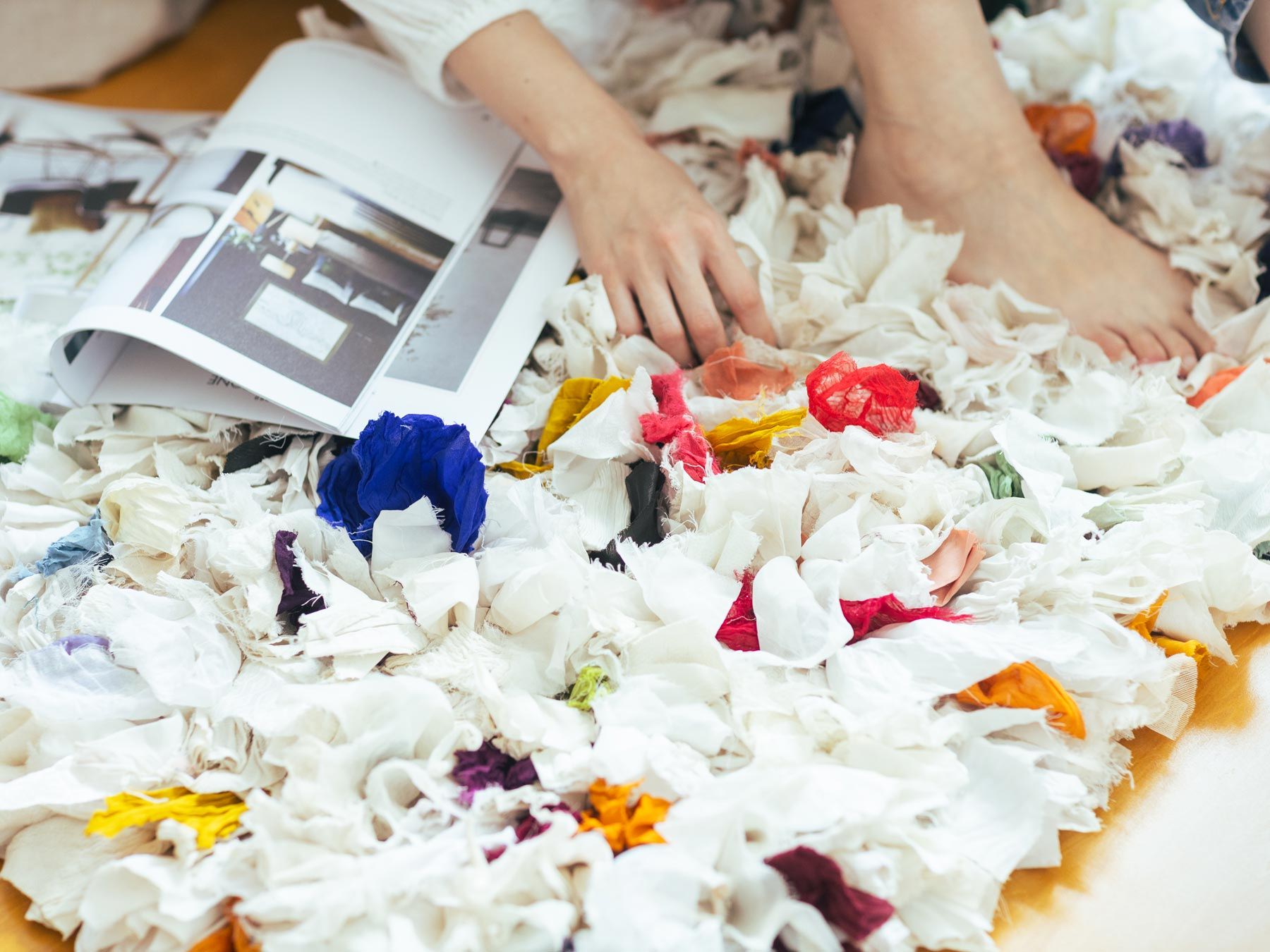 Person's hands and feet on a colorful, textured surface with a magazine.