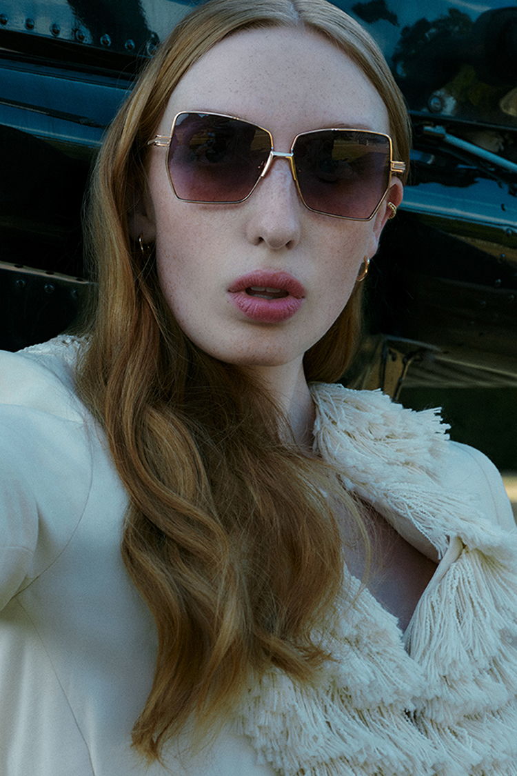 Young woman with long hair wearing sunglasses and a stylish coat.