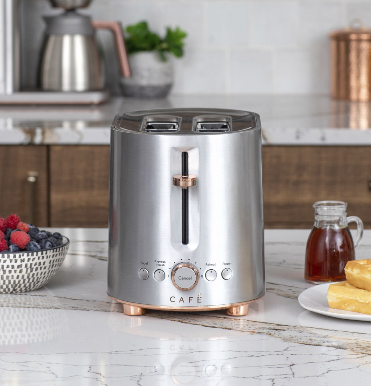 A stainless steel toaster on a marble countertop with fruit and syrup.