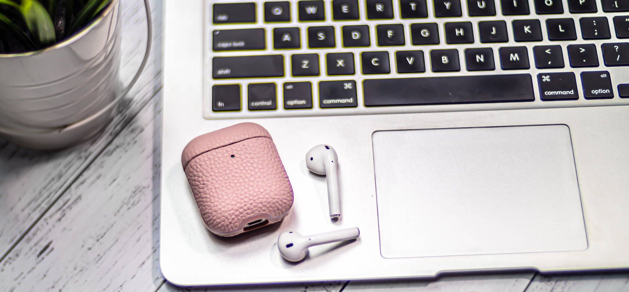 pink genuine leather airpods leather case laying on a silver macbook air and grey wooden table top